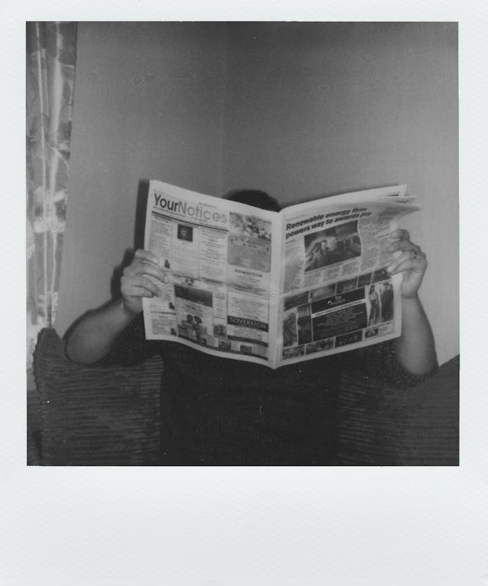 our-experience Person reading a newspaper at home in a vintage black and white style.